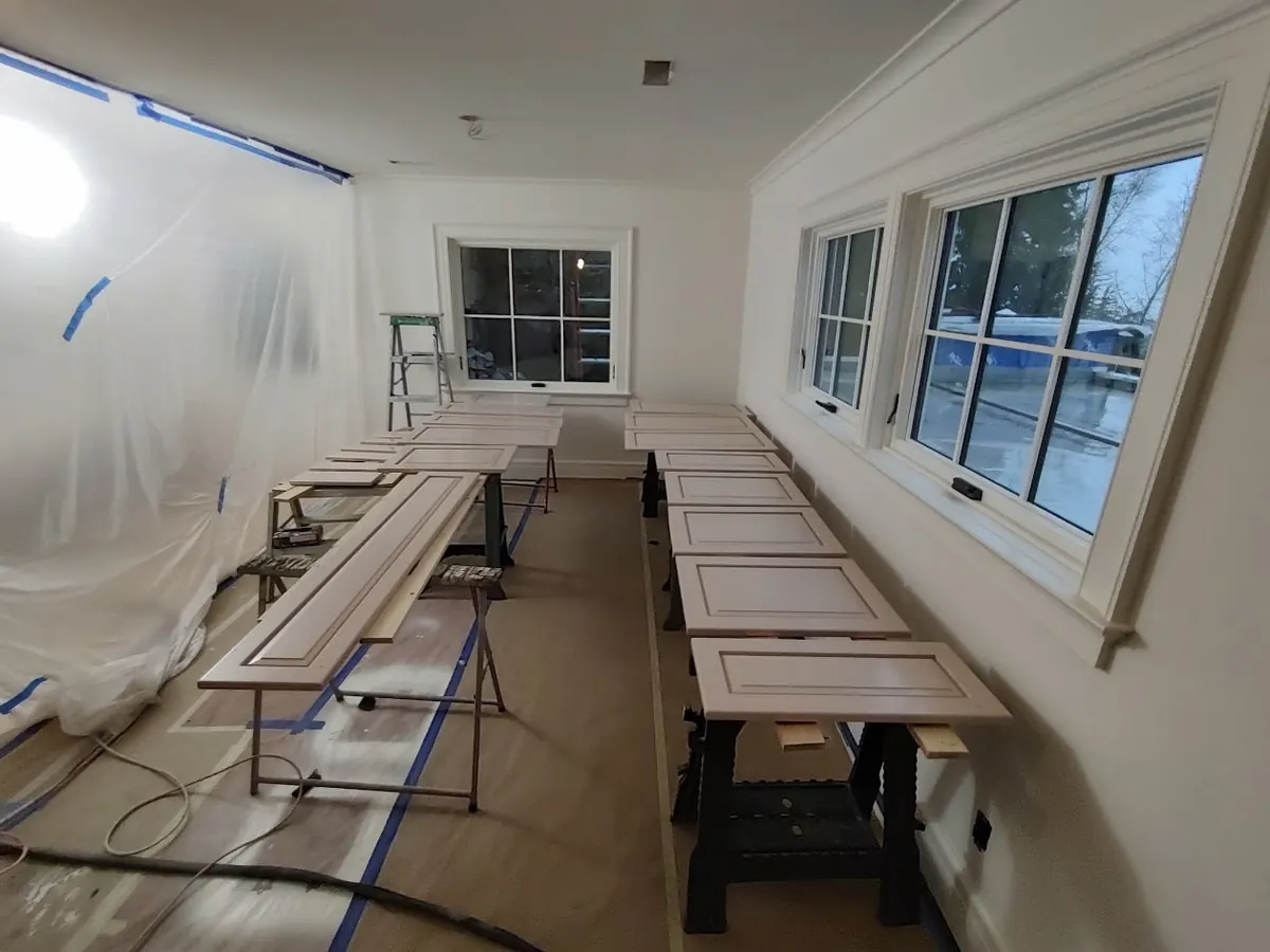 Rows of freshly sprayed cabinet doors curing on stands in a masked-off room