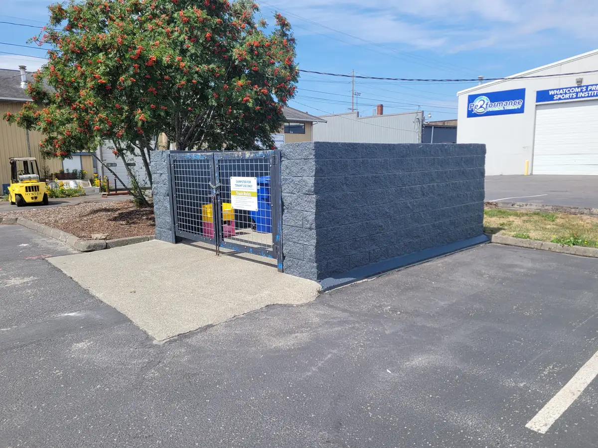 Block dumpster enclosure at a commercial lot, repainted charcoal